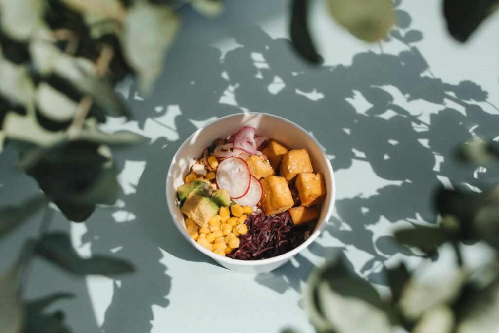 Top view of a vibrant poke bowl with tofu, avocado, and vegetables, surrounded by natural shadows.