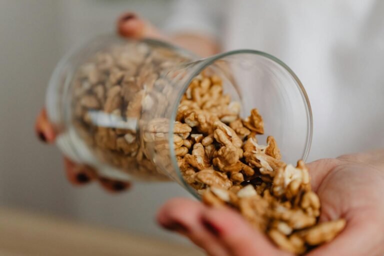 Hands pouring walnuts from a glass jar, featuring a rustic kitchen scene.