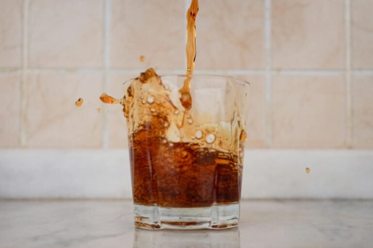 Dynamic shot of brown liquid splashing in a glass on a tiled background.