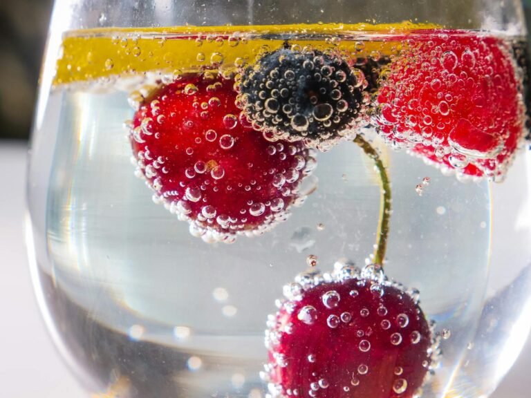 Close-up of fresh berries and lemon slice in sparkling water with bubbles.