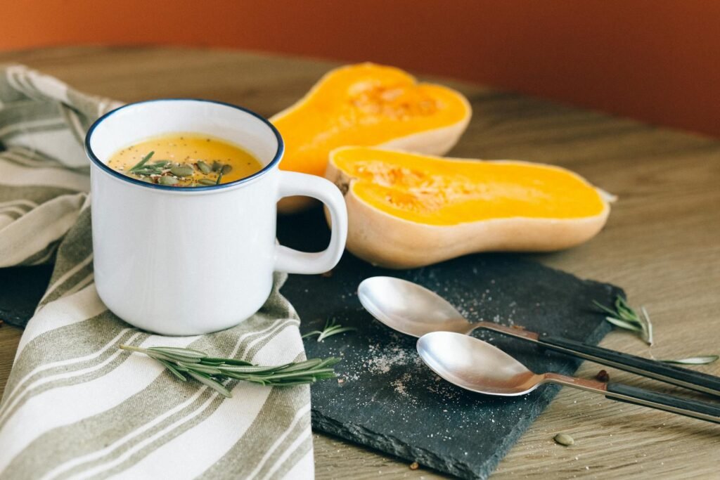 A cozy setting with butternut squash soup in a mug, complemented by fresh ingredients and rustic decor.
